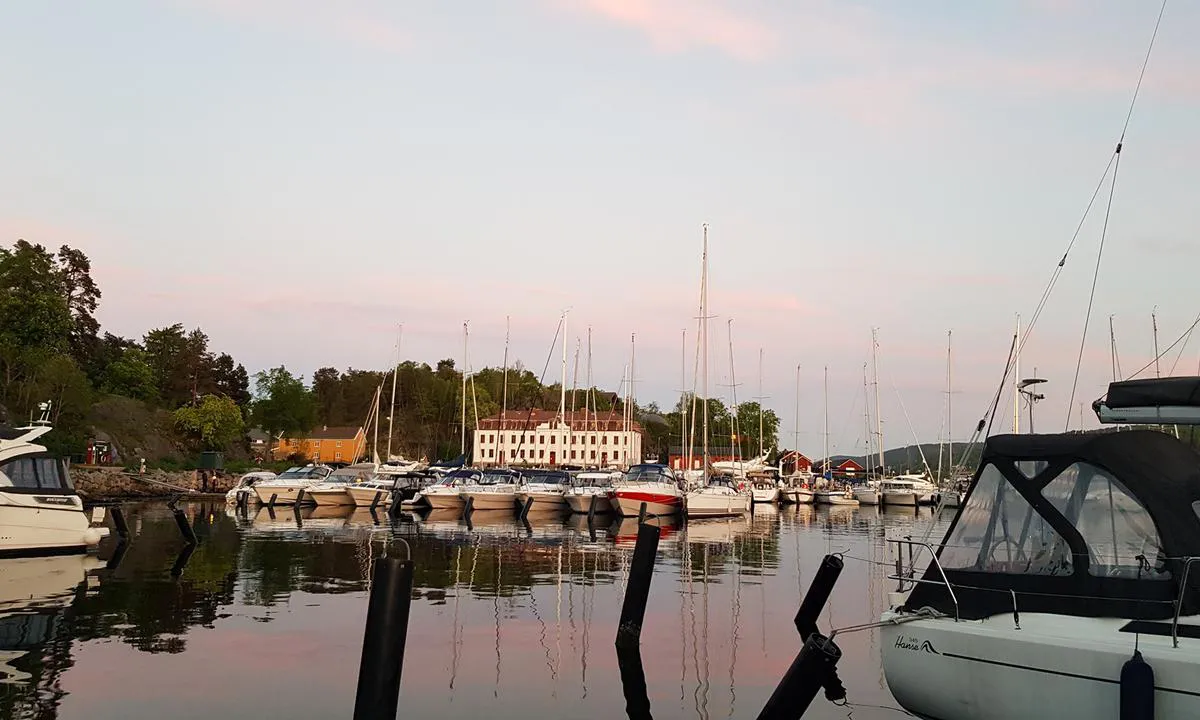 Oscarsborg Gjestehavn: Fra Steinbrygga på Nordre K. mot det gamle undervisningsbygget på Søndre.
Drøbak rett på andre siden av fjorden til venstre, adkomst inn i havnen til høyre.
Rett bak delvis synlig båt til venstre ligger bryggerestauranten.